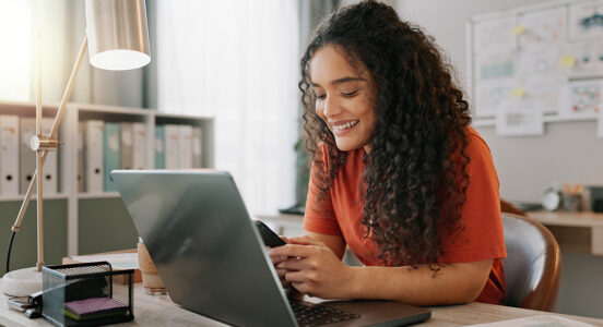woman on her phone looking at a computer on a desk