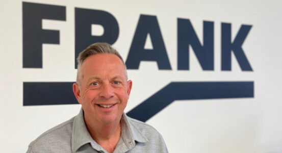 Graham Goodkind, founder and chairman of Frank PR, stands in front of the Frank logo.